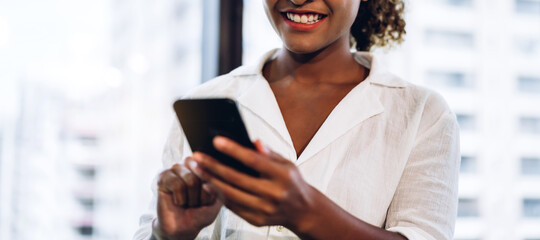 Smiling beautiful professional business african american black woman working and using smartphone standing in office