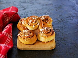 Wall Mural - Swedish twisted cinnamon rolls sprinkled with pearl sugar on a wooden board on a dark concrete background