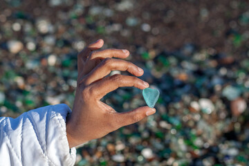 A brown indian hand holding a light glass piece shaped as heart by sea