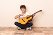 © luismolinero - Young caucasian man with a guitar sitting on the floor and pointing it