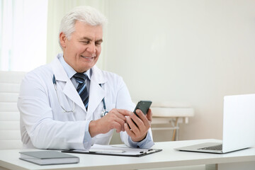 Canvas Print - Senior doctor with smartphone at table in office