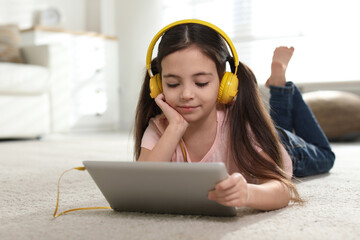 Wall Mural - Cute little girl with headphones and tablet listening to audiobook at home