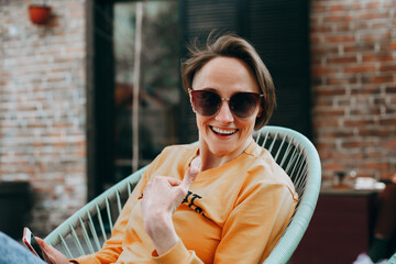 Sexy blonde young woman with short hair in sunglasses posing in the yard over brick wall background.