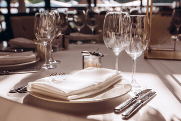 Wall Mural - Table setting for a wedding party. a round table with a white tablecloth, glasses, white plates in the rays of the setting sun.