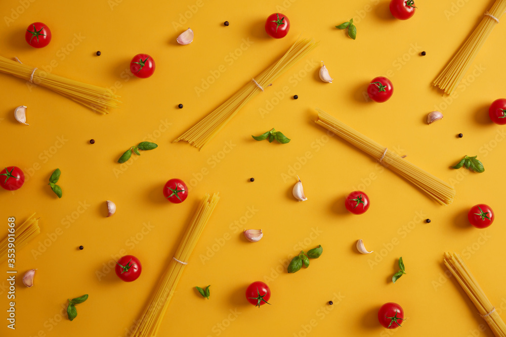 Raw ingredients for making pasta. Spaghetti, tomatoes, garlic and basil leaves. Herbs and spices for Italian food. Meal preparation. Yellow background. Cooking homemade delicious cuisine. Eating - obrazy, fototapety, plakaty 