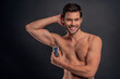© Roman - Handsome young man isolated. Portrait of shirtless muscular man is standing on grey background and using antiperspirant. Men care concept.