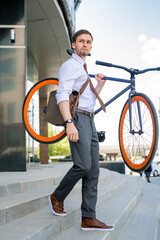 Canvas Print - Young businessman leaving office building after work and carrying his bicycle