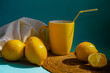 Lemons and a yellow mug with lemonade and a napkin in on a blue background and a ray of sunshine