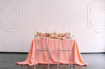 Banquet, restaurant. Table setting. Pink plates, gold cutlery, glasses. On the table is a pink tablecloth. Peach-colored napkin with a golden ring. Floral arrangements in peach pink hues. Tall candles