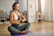 © Drazen - Smiling athletic woman meditating in lotus position at home.