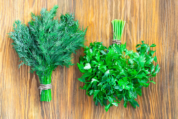 Two bunches of green parsley and dill in in yin and yang position on textured wooden brown background. Horizontal. Fresh spices from garden, Vegan ingredient and healthy food. Top view