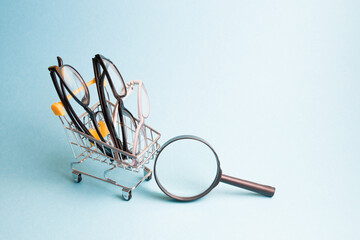 a few pairs of glasses in a small shopping cart, a magnifier on a light blue background, searching for glasses, buying glasses and eyeglass frames via the Internet