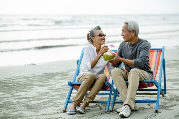 Romantic of senior happy couple sitting in deckchair on the beach together near sea and holding drinking coconut ,.Retirement age concept and love, copy space for text