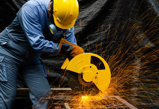 Worker cuts metal by electric circular saw. Fountain of grinding metal sparks. Metal working with personnel protective equipment..