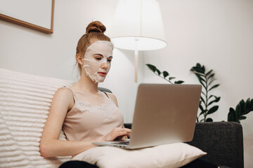 Wall Mural - caucasian woman with red hair wearing a paper mask on her face while lying in bed and using a laptop