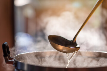 Wall Mural - The chef in the restaurant is cooking while using the dipper in a large pot. The water is boiling and the mass of steam reflected in the morning light.