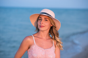 Young girl on vacation by the sea. Sunset at sea. Happy young woman in a dress and with a hat walks on the coast. Family context. Travel and Relax