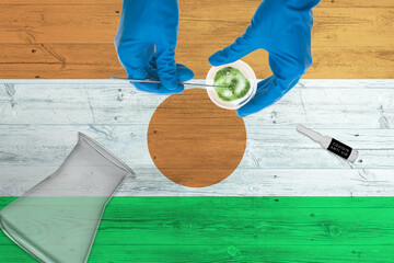 Wall Mural - Niger flag on laboratory table. Medical healthcare technologist holding COVID-19 swab collection kit, wearing blue protective gloves, epidemic concept.