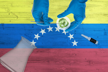 Wall Mural - Venezuela flag on laboratory table. Medical healthcare technologist holding COVID-19 swab collection kit, wearing blue protective gloves, epidemic concept.