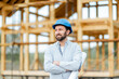 © rh2010 - Portrait of an architect or builder in hard hat standing in front of the wooden house structure. Building and designing wooden frame house concept