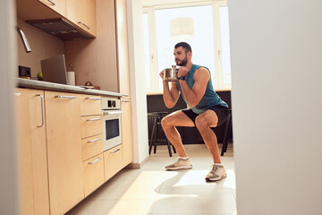 Wall Mural - Smiling gentleman doing squats and lifting cooking pot in kitchen