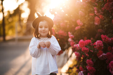 Wall Mural - Smiling cute baby girl 3-4 year old wearing stylish summer clothes and having fun over roses at background outdoors in city street. Looking at camera. Childhood. Summer season.