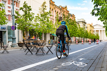 Rider cycling on the road bike in Vilnius city center reopening with open air restaurant and bar during Covid or Coronavirus emergency, sustainable transport concept