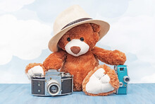 Stuffed Toy Teddy Bear In Hat Sitting And Holds Old Photo Camera And Retro Video Camera On A Blue Sky Background