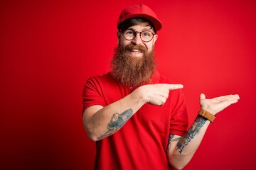 Canvas Print - Young handsome delivery man wearing glasses and red cap over isolated background amazed and smiling to the camera while presenting with hand and pointing with finger.