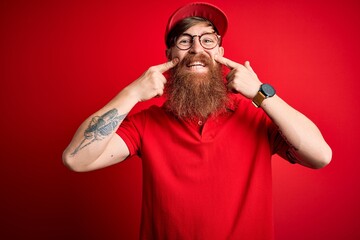 Wall Mural - Young handsome delivery man wearing glasses and red cap over isolated background Smiling with open mouth, fingers pointing and forcing cheerful smile