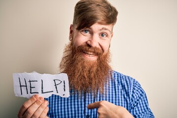 Sticker - Redhead Irish man with beard holding paper with help message over blue background with surprise face pointing finger to himself