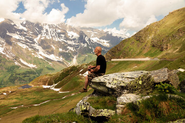 Man on top of mountain. Conceptual design. An elderly man sits on top of a mountain. Active holiday in retirement. Time is one with itself. Mountain landscape in the Alps.