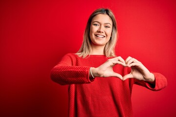 Poster - Young beautiful blonde woman wearing casual sweater over red isolated background smiling in love doing heart symbol shape with hands. Romantic concept.