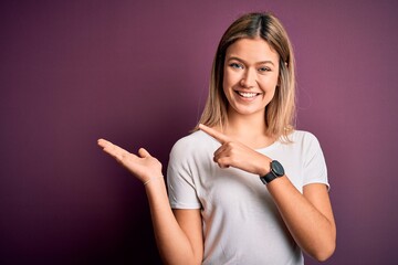 Poster - Young beautiful blonde woman wearing casual white t-shirt over purple isolated background amazed and smiling to the camera while presenting with hand and pointing with finger.