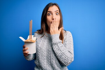 Poster - Young woman eating asian noodles from take away box using chopstick over blue background cover mouth with hand shocked with shame for mistake, expression of fear, scared in silence, secret concept