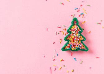 Christmas celebration flat lay with toy christmas tree and sprinkle on pink background