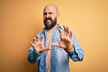 Wall Mural - Handsome bald man with beard wearing casual denim jacket and striped t-shirt disgusted expression, displeased and fearful doing disgust face because aversion reaction. With hands raised