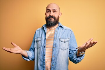 Sticker - Handsome bald man with beard wearing casual denim jacket and striped t-shirt clueless and confused expression with arms and hands raised. Doubt concept.