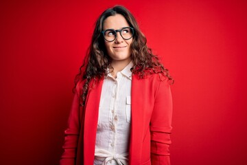 Sticker - Young beautiful woman with curly hair wearing jacket and glasses over red background smiling looking to the side and staring away thinking.