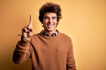 Young handsome man wearing casual shirt and sweater over isolated yellow background pointing finger up with successful idea. Exited and happy. Number one.