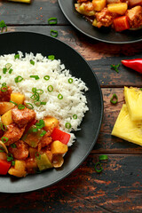 Wall Mural - Pineapple and Chicken in sweet and sour sauce with bell pepper, rice and spring onion in black plate