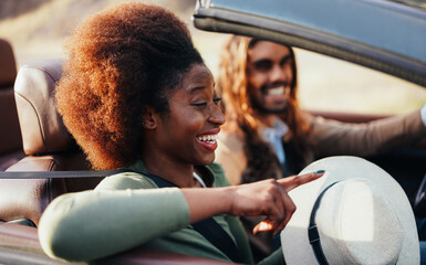 Happy people having fun in convertible car in summer vacation - Young couple enjoyng  holiday on cabriolet auto outdoor - Travel, youth lifestyle and wanderlust concept - Focus on afro girl eye