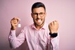 Young real estate business man holding new house keys over pink background annoyed and frustrated shouting with anger, crazy and yelling with raised hand, anger concept
