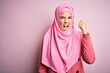 © Krakenimages.com - Young beautiful girl wearing muslim hijab standing over isolated pink background angry and mad raising fist frustrated and furious while shouting with anger. Rage and aggressive concept.