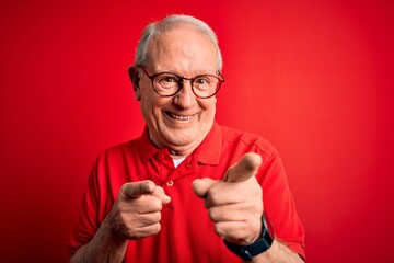 Grey haired senior man wearing glasses and casual t-shirt over red background pointing fingers to camera with happy and funny face. Good energy and vibes.