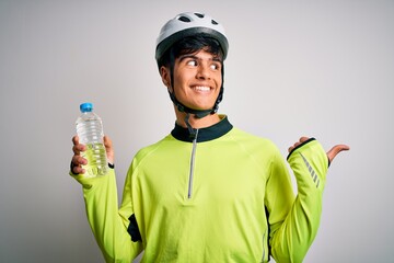 Poster - Young handsome cyclist man wearing security bike helmet drinking bottle of water pointing and showing with thumb up to the side with happy face smiling