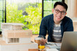 © whyframeshot - smart smile asian architect interior designer working house design project with home mockup and blueprint paper and material chart sample with enthusiasm focus and confident with garden background