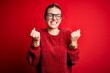 Young beautiful redhead woman wearing casual sweater over isolated red background very happy and excited doing winner gesture with arms raised, smiling and screaming for success. Celebration concept.