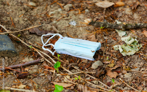Facial surgical mask used and thrown away on the ground in the park. True and authentic image of a dirty mask.