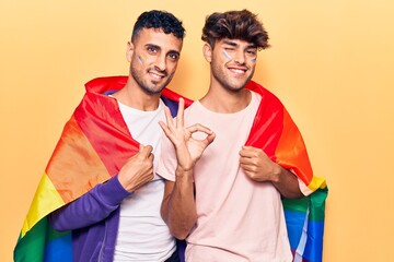 Poster - Young gay couple wearing rainbow lgbtq flag doing ok sign with fingers, smiling friendly gesturing excellent symbol